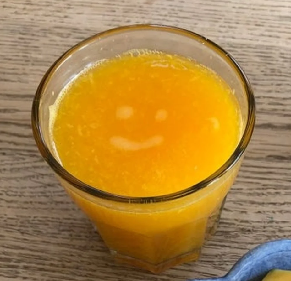 Pohár pomarančového džúsu s úsmevom na povrchu, položený na drevenom stole.