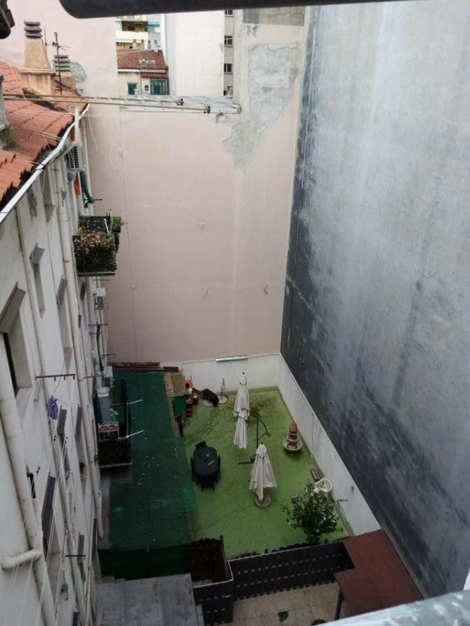 Uzavretý dvor medzi vysokými budovami s trávnikom, stolom a slnečníkmi.