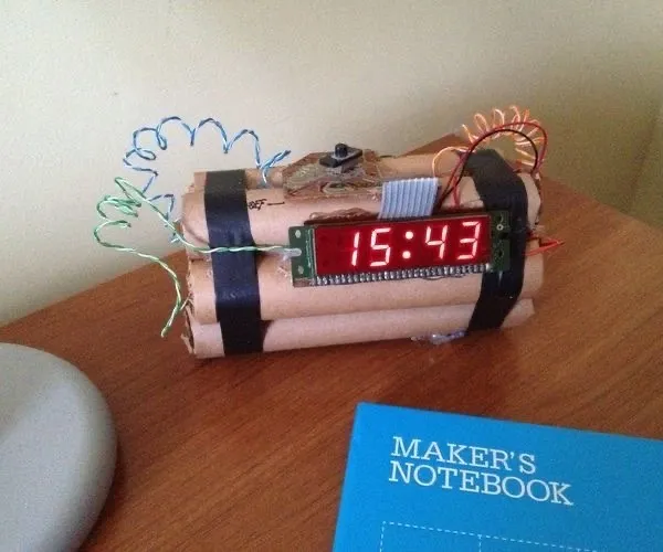 Zostrojené zariadenie na stole s digitálnym časom 15:43 a poznámkovým blokom Maker's Notebook.