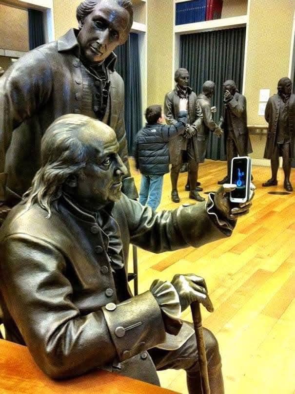 Socha v starodávnom oblečení drží mobilný telefón v múzeu, moderná technológia versus história.