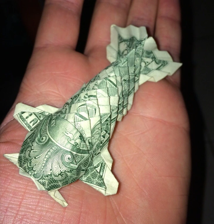 Origami ryba zložená z dolárovej bankovky na otvorenej dlani.