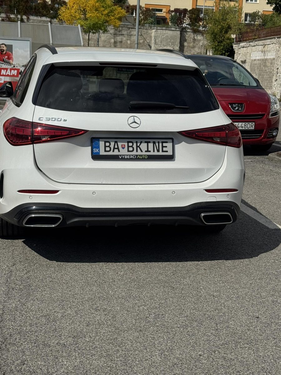 Biele auto Mercedes s poznávacou značkou BABKINE zaparkované na parkovisku za slnečného počasia.