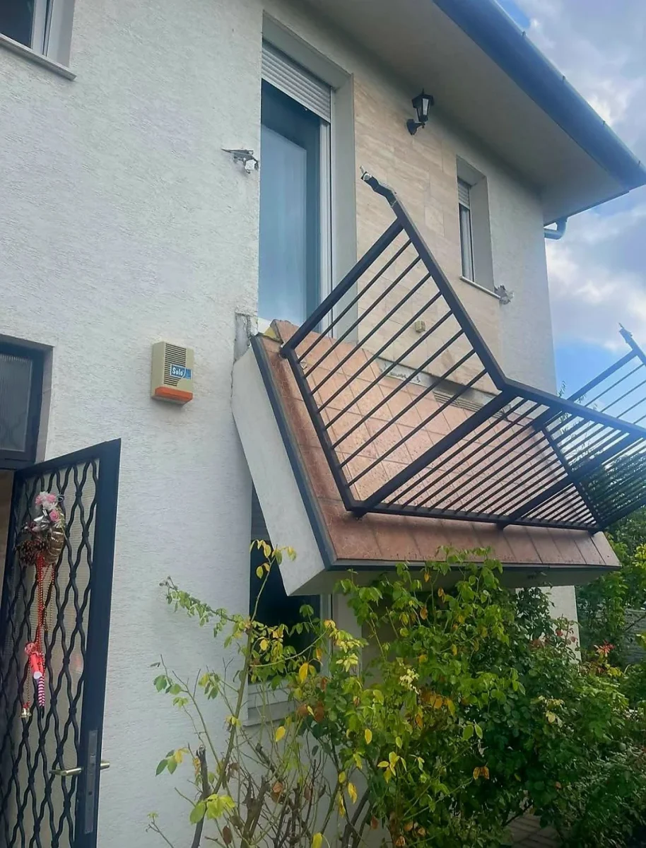 Balkónová zábradlie sa zrútilo pred oknom na boku domu, obklopené zeleným lístím.