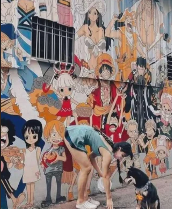 Žena so psom pred farebnou stenou s anime postavami, vytvára veselú atmosféru ulice.