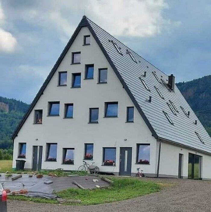 Moderný trojuholníkový dom s množstvom okien a šedou strechou, umiestnený v prírodnom prostredí.