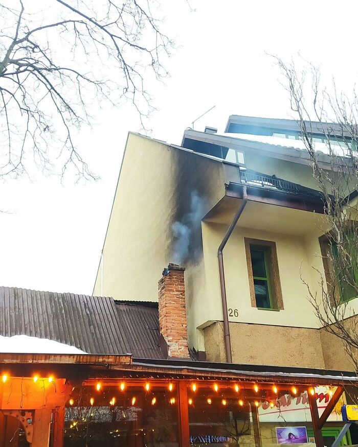 Komín na dome s čiernymi sadzami a ľahkým dymom, zimné osvetlenie v popredí.