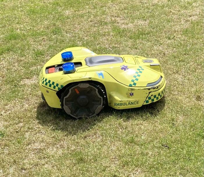 Žltá robotická kosačka na trávu v štýle sanitky s modrými svetlami na zelenej tráve.