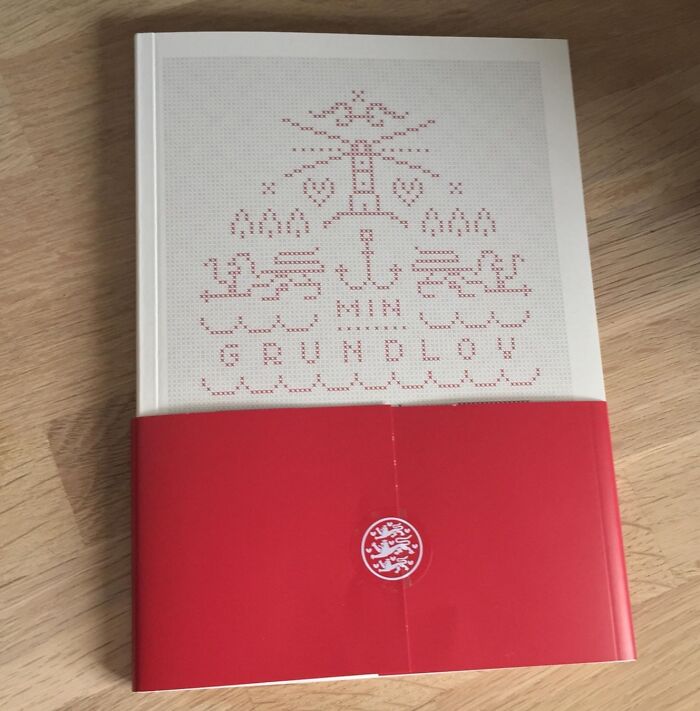Kniha s nápisom Min Grundlov na drevenom stole, červený obal s jednoduchým vzorom.