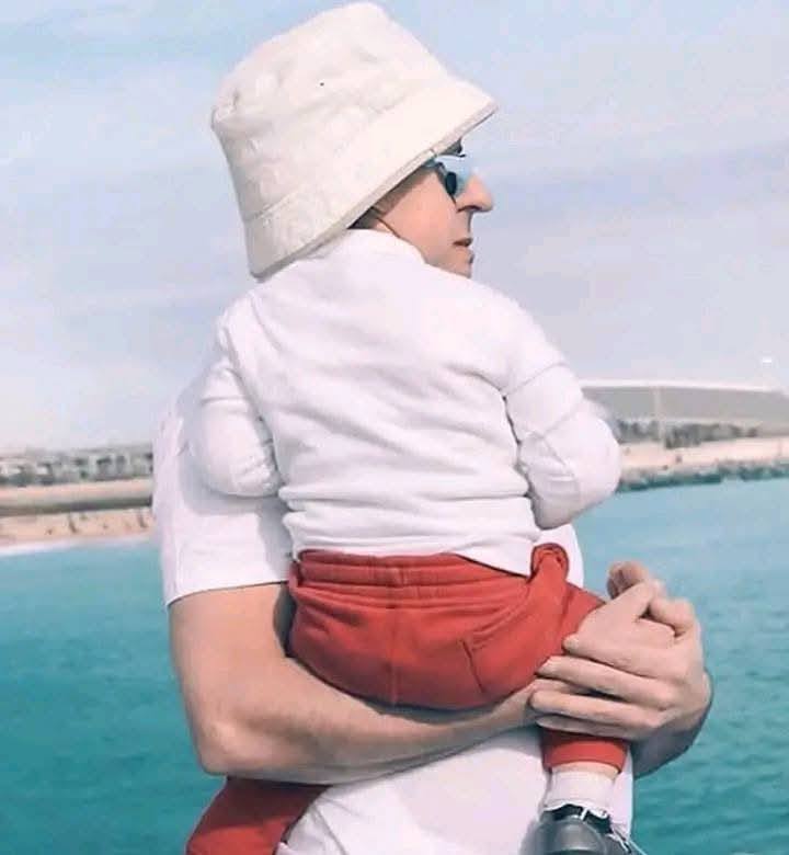 Dospelý drží dieťa tak, že sa ich tváre v pohľade fotoaparátu prekrývajú.
