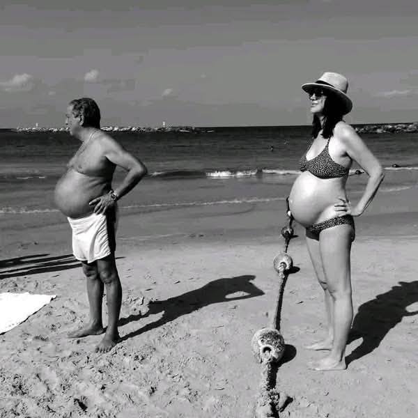 Dvaja ľudia stoja na pláži v podobnej póze s rukami pri bokoch.