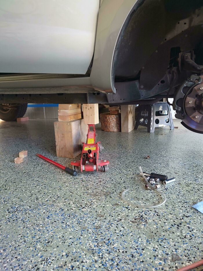 Auto na zdvihákoch v garáži, obklopené náradím a drevenými klátikmi, príprava na opravu podvozku.