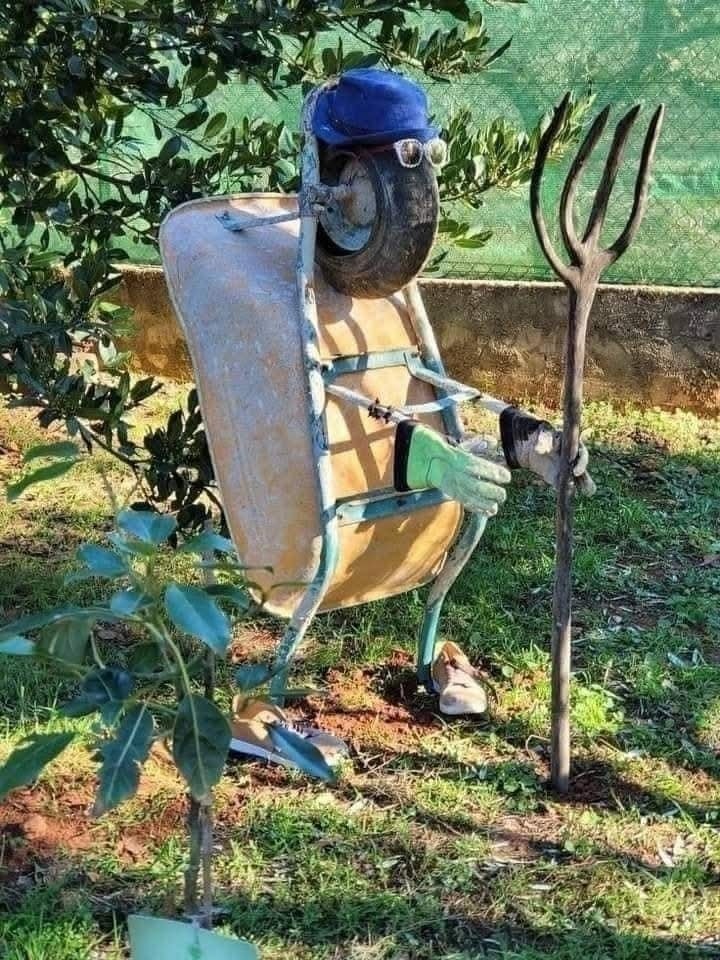 Kreatívna socha z fúrika a náradia imitujúca farmára na záhrade.
