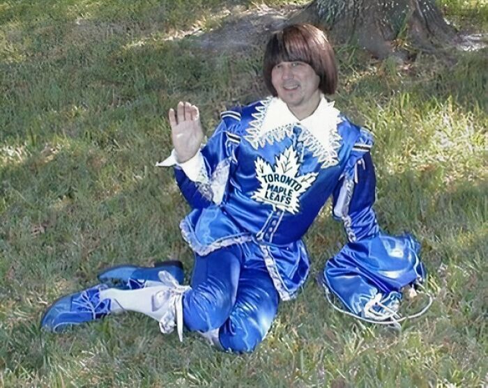 Osoba v modrom historickom kostýme s logom Toronto Maple Leafs pózuje na tráve s úsmevom.