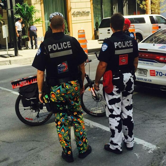 Policajti v pestrofarebných nohaviciach stojaci na ulici pri bicykli a policajnom aute.