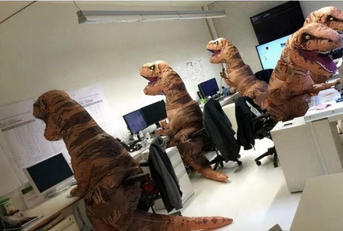Dinosaury v kancelárii sedia pri počítačoch, veselá pracovná atmosféra.
