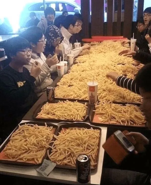 Skupina ľudí si užíva veľkú množinu hranoliek vo fastfoode, stôl pokrytý tacami plnými hranoliek.