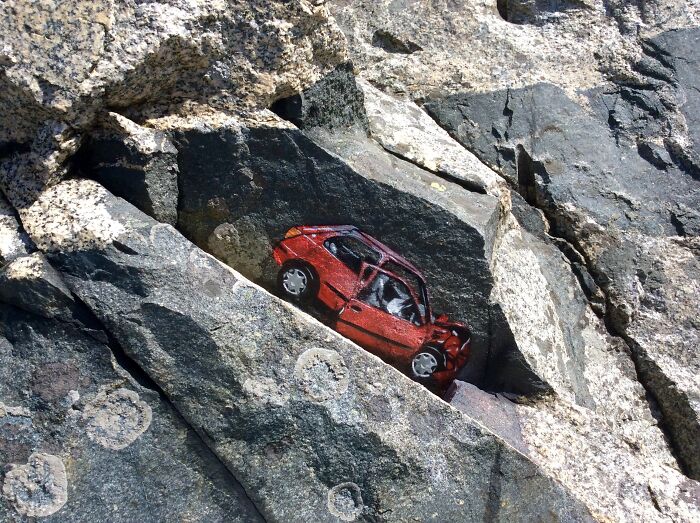 Červené auto zanechané medzi skalami v prírode, zabudnutá história na neobyčajnom mieste.