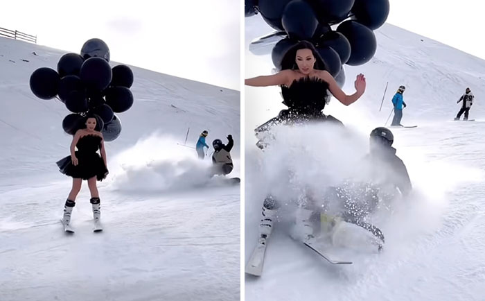 Žena s balónmi v čiernych šatách na svahu, zatiaľ čo snowboardista prechádza okolo, spôsobujúc oblak snehu.