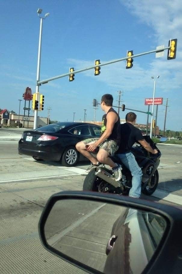Muž sediaci opačne na motocykli na križovatke, vedľa čierneho auta, zelená svetlá na semafore.