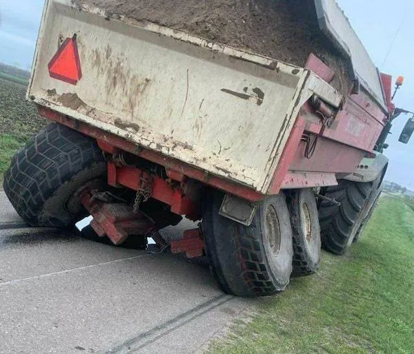 Traktor s nákladom hliny sa zakliesnil na úzkej ceste, blízko koleso v jarku.