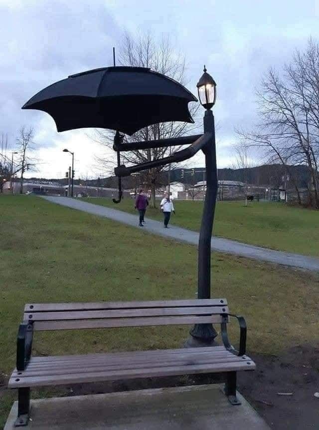 Pouličná lampa s čiernym dáždnikom a lavičkou v parku, zábavný mestský dizajn.