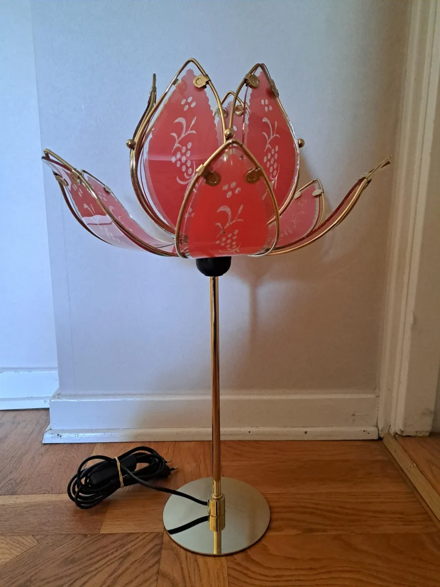 Stolná lampa v tvare kvetu s ružovými zdobenými sklenenými lístkami a zlatým podstavcom na drevenej podlahe.