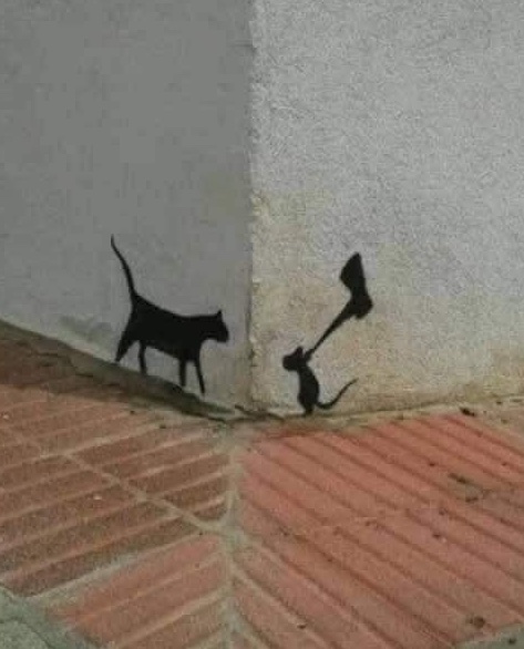 Graffiti na stene: mačka a myš s kladivom v humornom konflikte na rohu budovy.