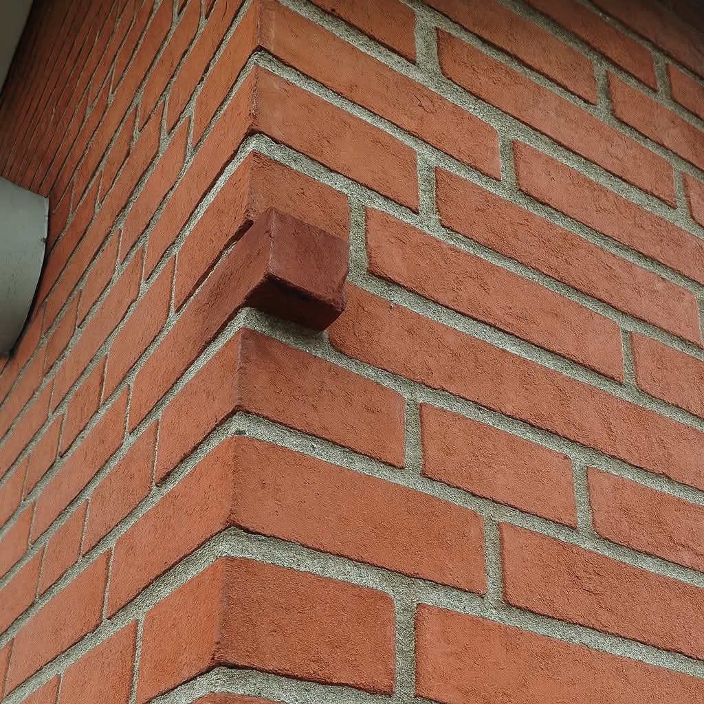 Roh tehlovej steny s nepravidelne vyčnievajúcou tehlou, detail architektonického dizajnu.