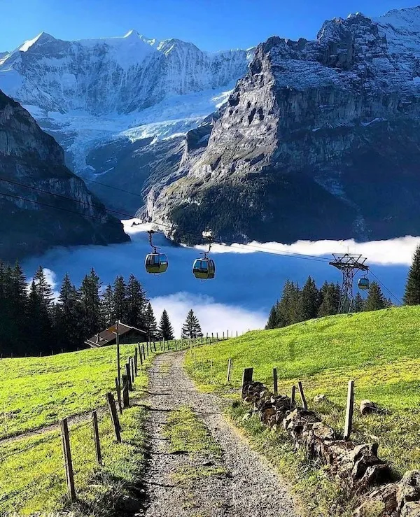 Lanovka nad údolím obklopeným horskými vrcholmi, zelenými lúkami a hmlou v panoramatickej horskej scenérii.