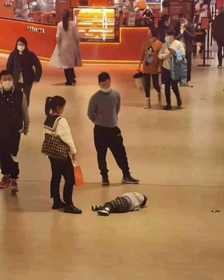 Dieťa leží na podlahe v priestore s obchodmi a ďalšími ľuďmi.