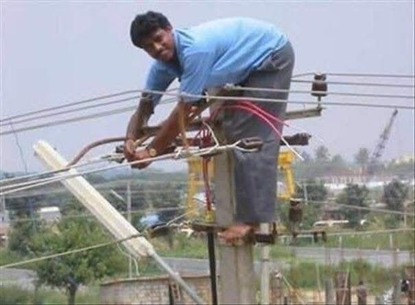 Elektrikár pracujúci na elektrickom stĺpe bez ochrany, ukážka nebezpečnej práce vo výške.