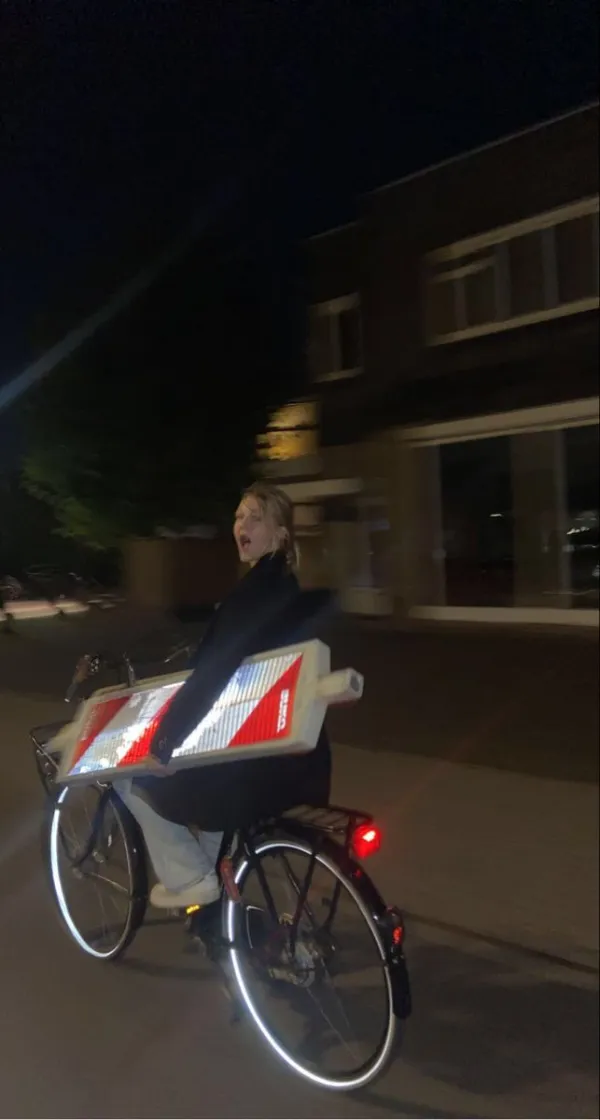 Osoba na bicykli v noci vezie veľkú dopravnú značku, vyjadruje prekvapenie.