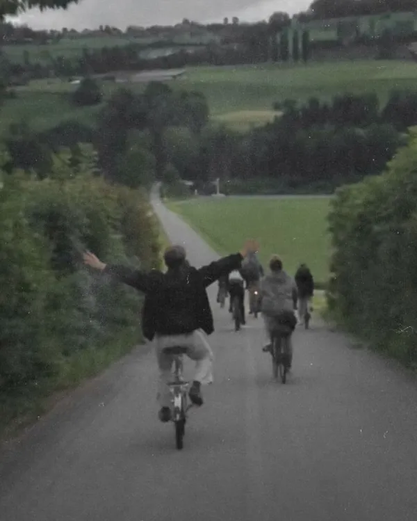 Skupina cyklistov sa teší z jazdy po vidieckej ceste obklopenej zelenými lúkami a stromami.