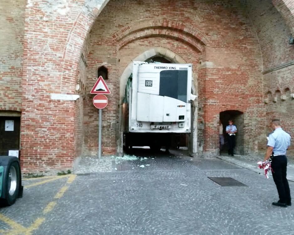 Nákladné auto uviaznuté v úzkej bráne, obklopené dôstojníkmi, ktorí situáciu kontrolujú.