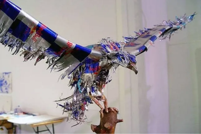 Socha orla z plechoviek v realistickej póze na konári, symbol kreatívneho využitia recyklovaných materiálov.