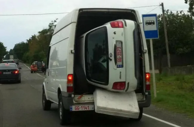 Dodávka prepravujúca malé auto vo vnútri, zaparkovaná pri ceste.