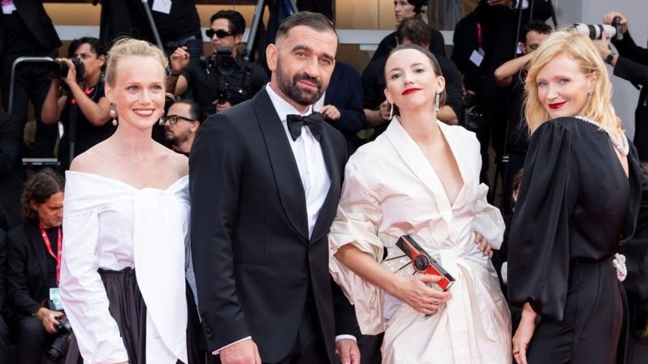 Ľudia na červenom koberci v elegantnom oblečení počas filmového festivalu, pózujú pred fotografmi.