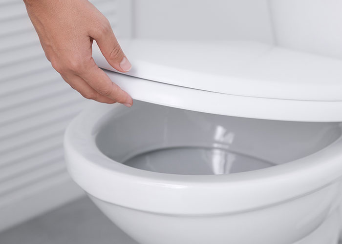 Ruka zatvára toaletné sedadlo v kúpeľni, zamerané na hygienu a udržiavanie čistoty.