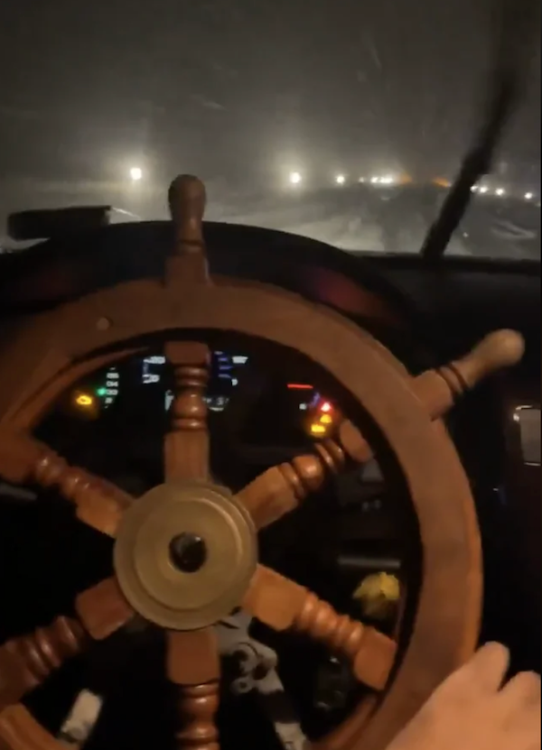 Volant v tvare lodného kormidla počas jazdy autom v noci. Zasnežená cesta a osvetlenie v diaľke.