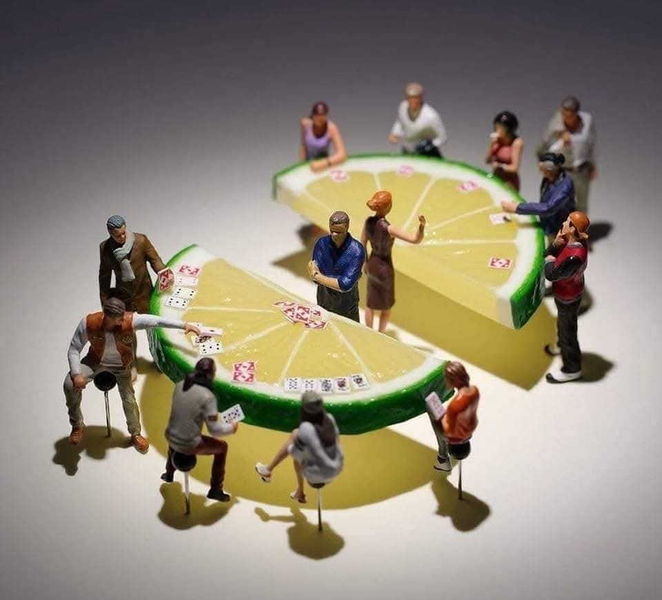 Miniatúrni ľudia hrajú poker na stoloch v tvare citrónových koliesok.