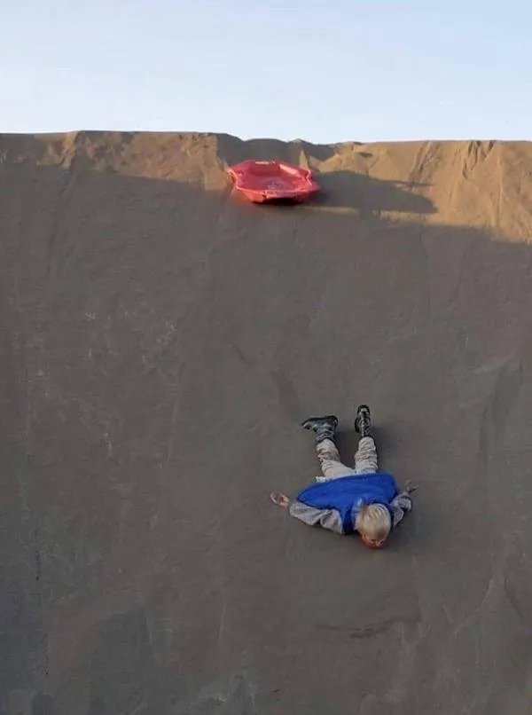 Osoba ležiaca na pieskovej dune po zábavnom zjazde na sánkach, pohodené na okraji.