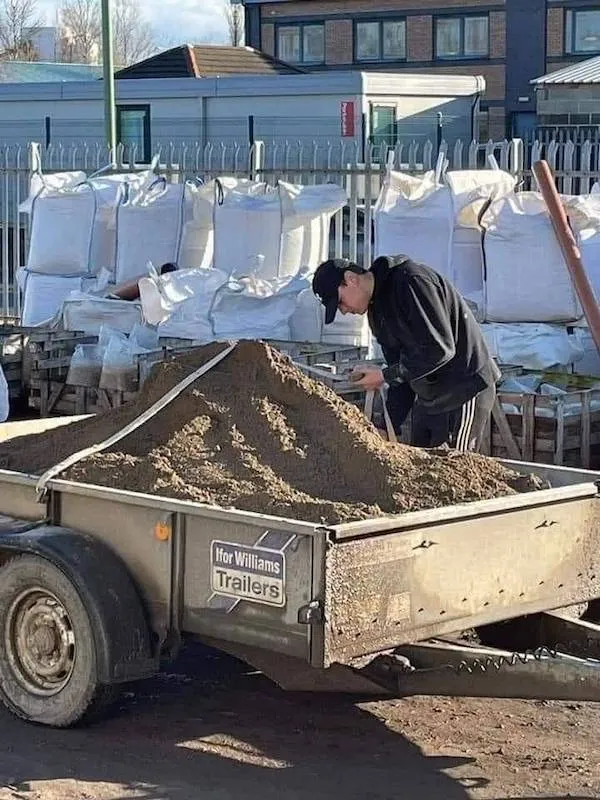 Muž v čiernom oblečení nakladajúci piesok na vozík na stavbe.