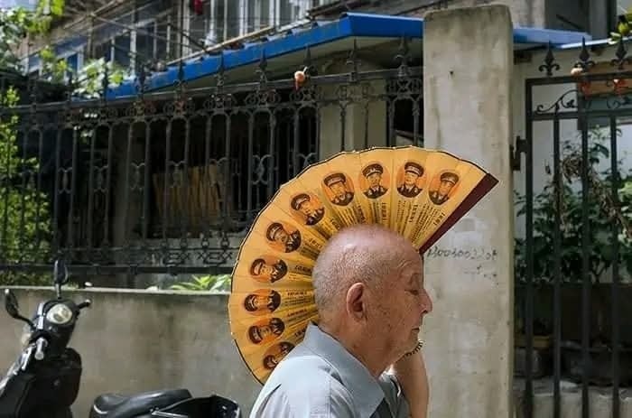 Muž s vejárom na hlave ako klobúk stojí pred budovou a motorkou.
