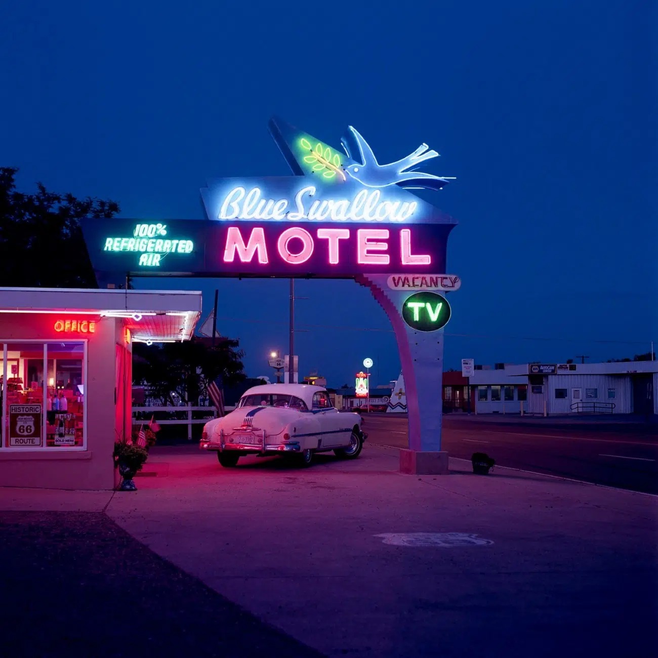 Nočný pohľad na retro motel Blue Swallow s neónovým nápisom a zaparkovaným klasickým autom.