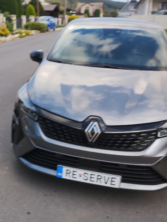 Strieborné auto značky Renault s poznávacou značkou RE SERVE zaparkované na vidieckej ulici.