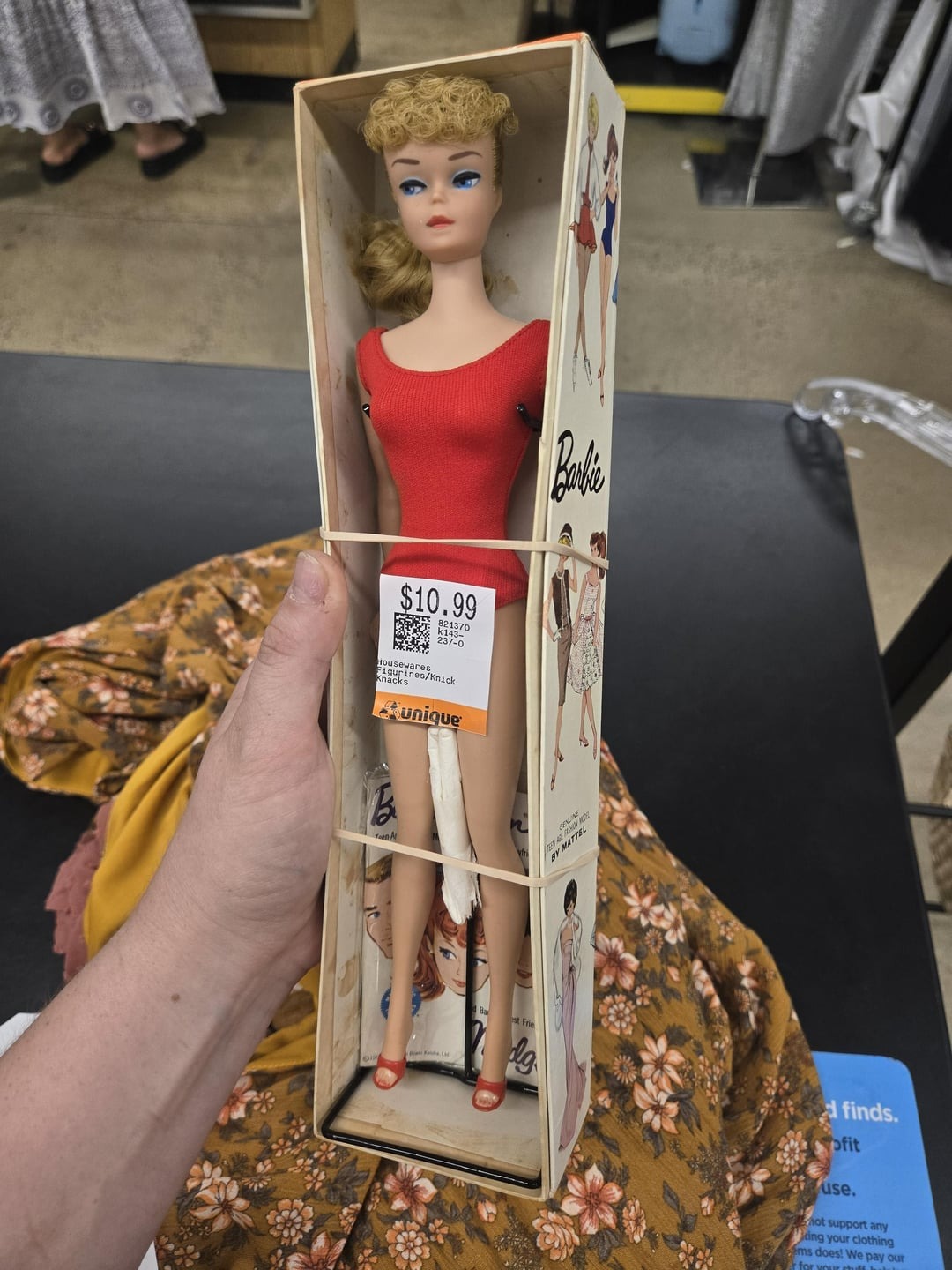 Vintage bábika v červenom outfite v pôvodnej krabičke, cena 10,99 dolárov, zobrazená na predajnom pulte obchodu.