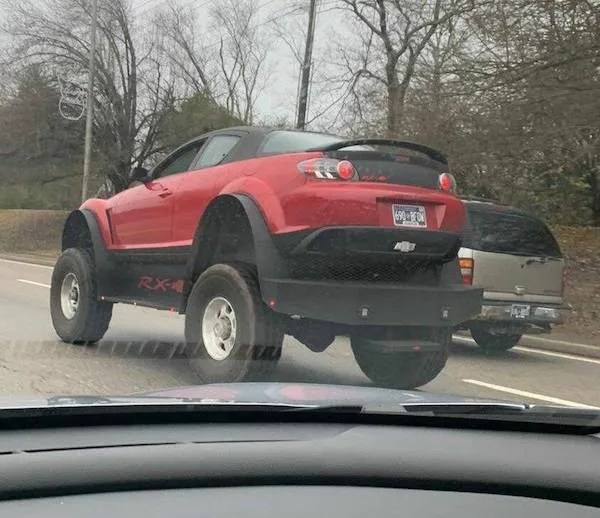 Červené auto s vysokým podvozkom na ceste, upravené pre extrémne terény.