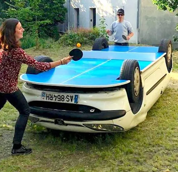 Ľudia hrajú stolný tenis na improvizovanom stole vyrobenom z prevráteného auta.