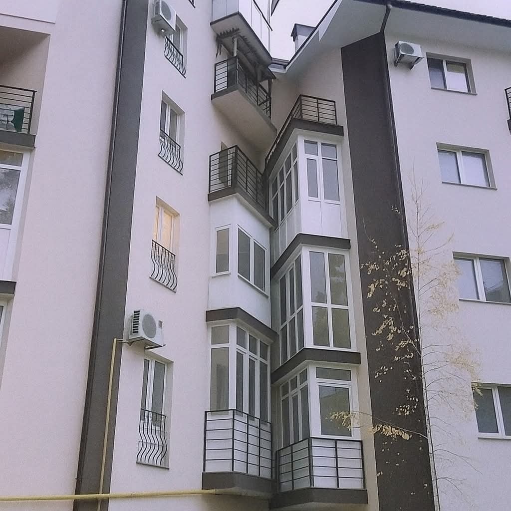 Moderná bytová budova s balkónmi a veľkými oknami, farebné na bielu a sivú, s klimatizačnými jednotkami.