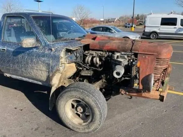 Starý pickup truck s odhaleným motorovým priestorom na parkovisku.